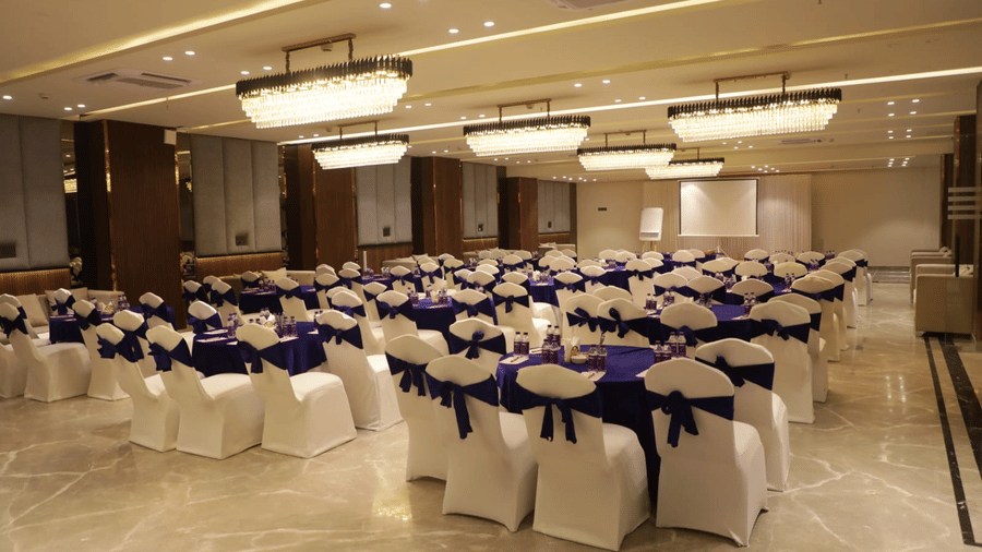 A banquet hall at Hotel 91 HUDA Premier, Gurugram with rows of chairs, tables, and ceiling lights arranged for an event.