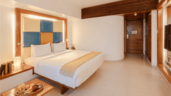 View of a room at The Promenade Pondicherry with a king bed, blue and yellow headboard panel, wooden nightstands, and warm ambient lighting.