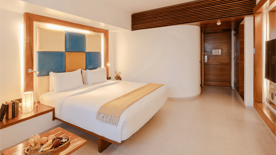 View of a room at The Promenade Pondicherry with a king bed, blue and yellow headboard panel, wooden nightstands, and warm ambient lighting.