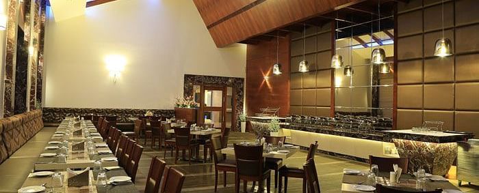A spacious restaurant with elegant wooden interiors, neatly arranged tables, and a warm ambient lighting design. - Dhanalakshmi Srinivasan Hotels, Perambalur