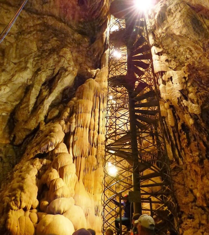 A circular staircase inside a cave with a light shining down the cave.