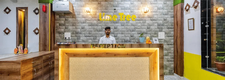 A hotel reception area with a wooden counter, yellow accents, and a stone-textured wall - Lime Tree Hotels & Banquet, Vrindavan