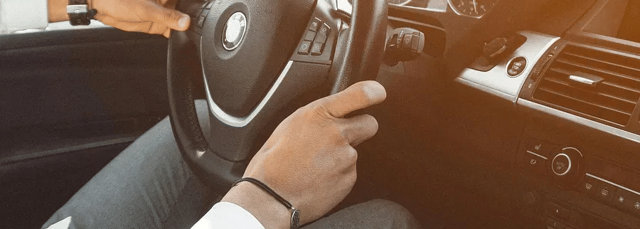 A person driving a car, with a focus on the steering wheel and dashboard.