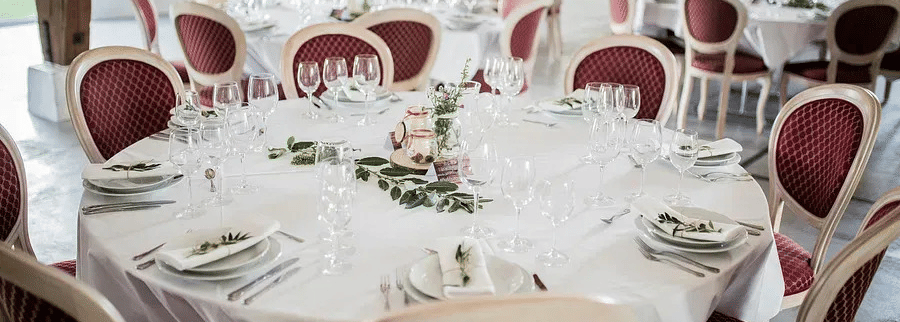 A banquet setup with round tables, white tablecloths, and neatly arranged cutlery and glasses.