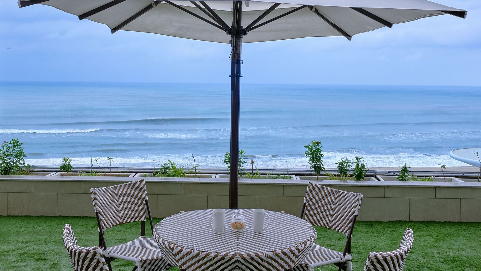 Sitting space with four chairs placed around a table of the Premium Room at Swosti Premium Beach Resorts in Puri with the view of the sea under a partially cloudy sky