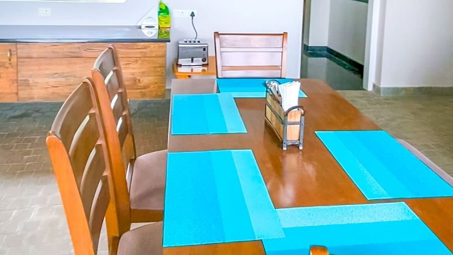 Dining area with long wooden table, colourful place-mats, wooden chairs and modern decor at Ibex Resorts, Coonoor (Tapas).