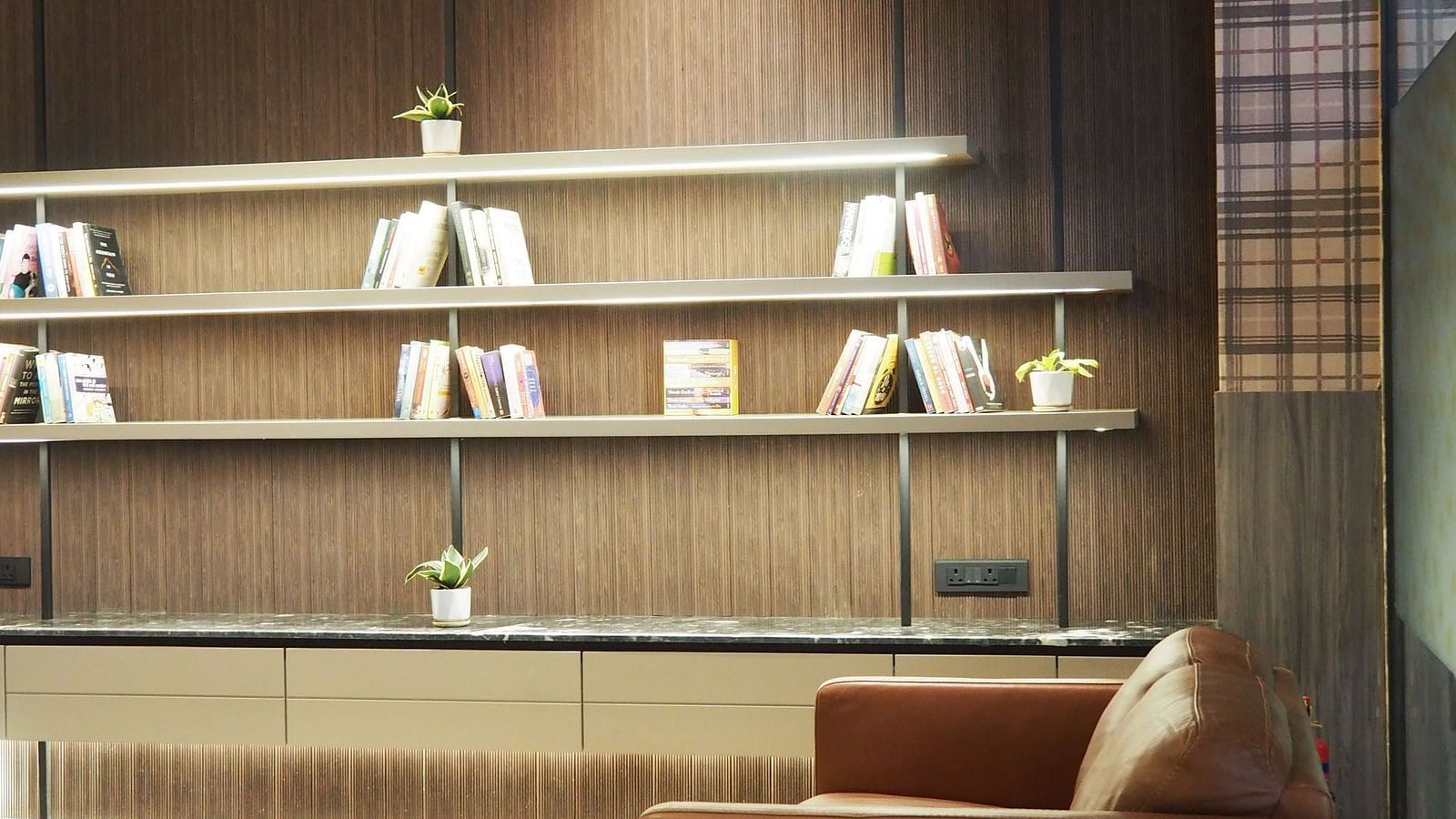 A modern room with two armchairs, a small table, and open shelves on a dark wall - Club Charholi, Pune 