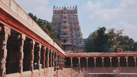 A temple pond with steps and pillars, featuring a five-tiered gopuram in Dravidian architectural style in the back - Grand Madurai by GRT hotels.