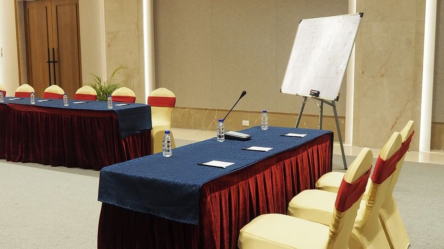 A long table with multiple chairs neatly arranged and a podium kept beside it with light-coloured walls - Club Charholi, Pune 