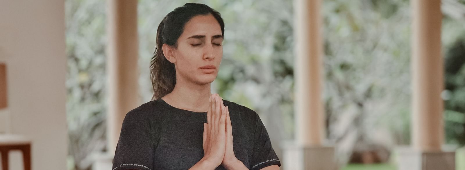A person doing yoga on a mat in a room with large windows and plants.