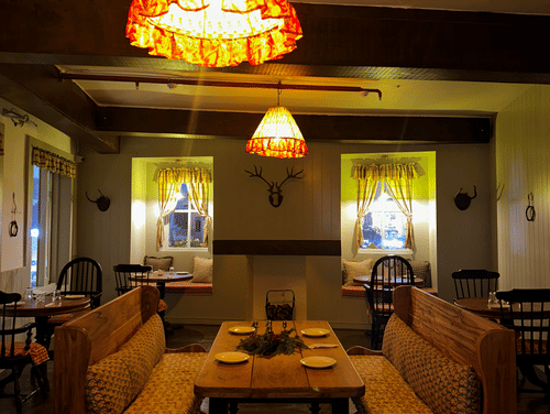 Image of a table with benches facing each other under a dim warm light giving out a rustic charm of Old England Cafe - Hotel Atulyaa Taj, Agra in the evening