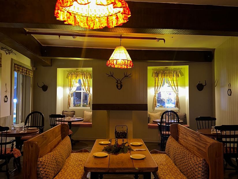 Image of a table with benches facing each other under a dim warm light giving out a rustic charm of Old England Cafe - Hotel Atulyaa Taj, Agra in the evening