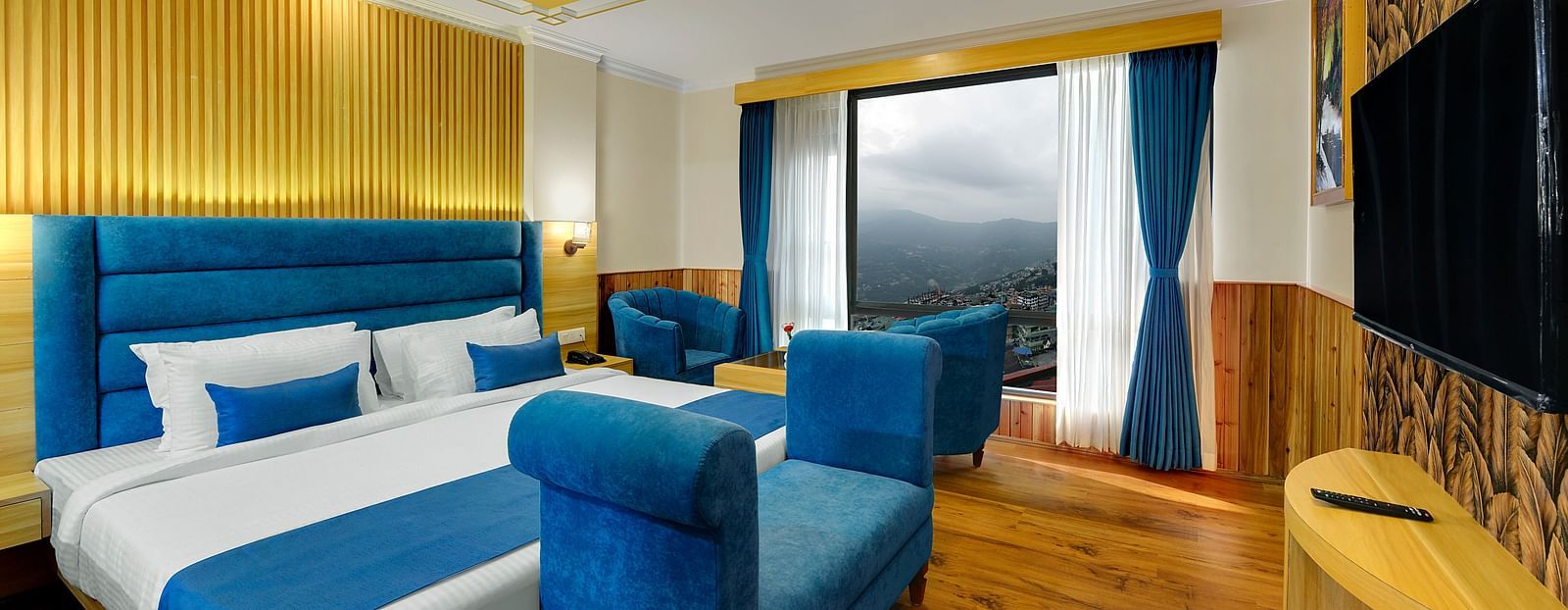 An image of the family suite at Yashshree Sikkim Blossom, Gangtok with a bed, a couch, a sofa set, a table, flat screen TV and an expansive window