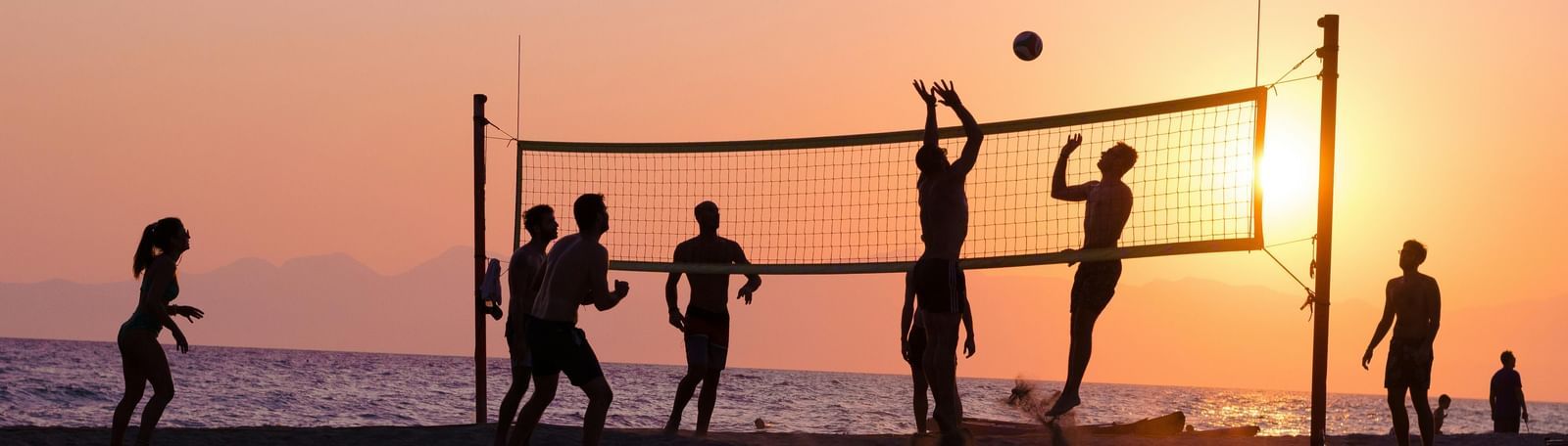 An image of group of friends enjoying volleyball by the beach during a sunset