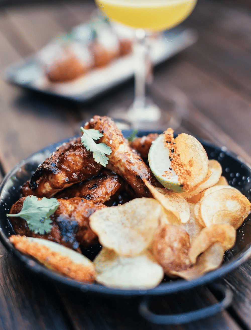 A close-up of crispy chicken wings with chips and a refreshing drink, available at the Tallman Hotel.