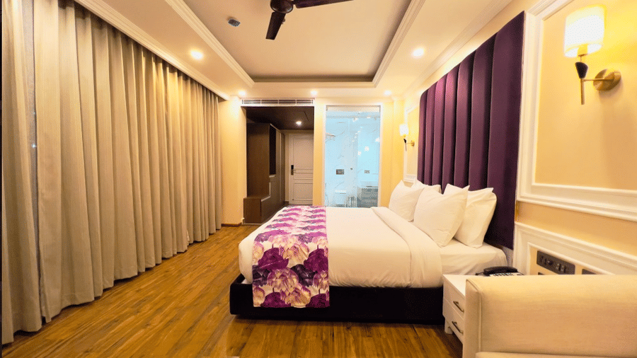 Claret Inn, Dalhousie - Rooms with balcony in Dalhousie with a bed, purple bed runner, white sofa, ceiling fan, and closed curtains.