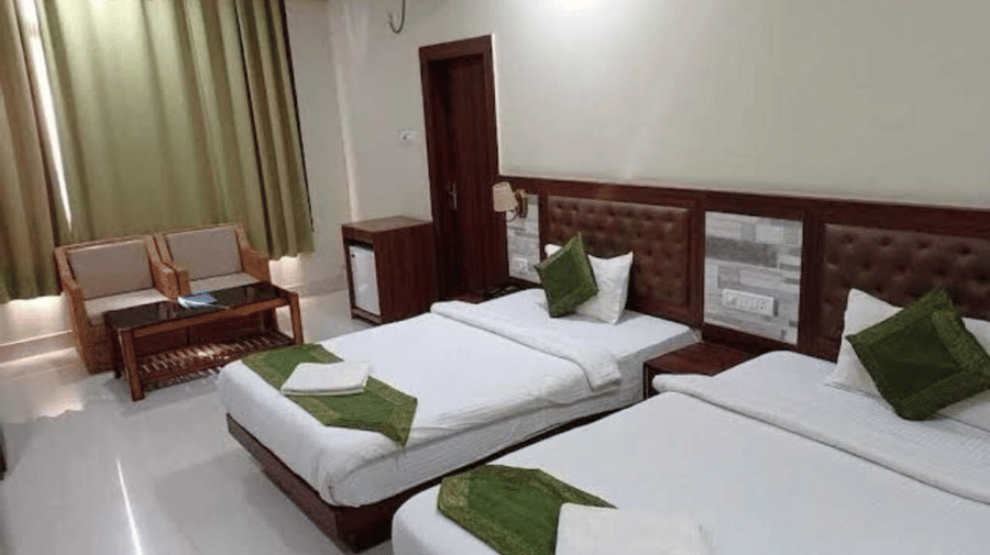 A bedroom with twin bed, seating area, white linen and green cushions, ideal for a comfortable and relaxed visit at Pemaling Lords Eco Inn Guwahati.