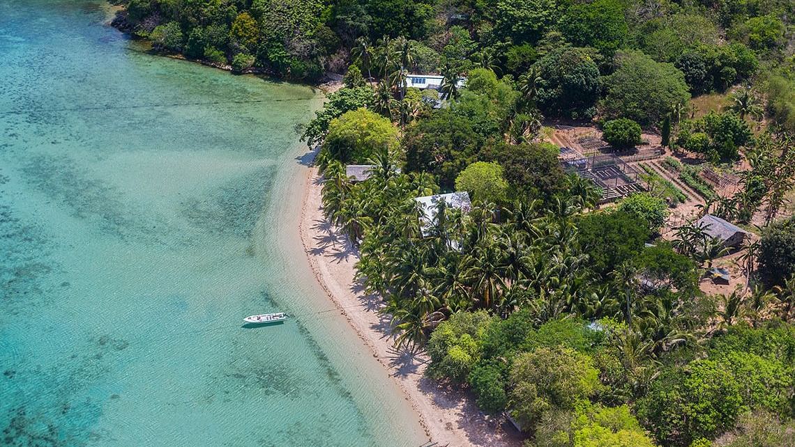 Coastal aerial view showing turquoise water, beach, and greenery at Flower Island Resort.
