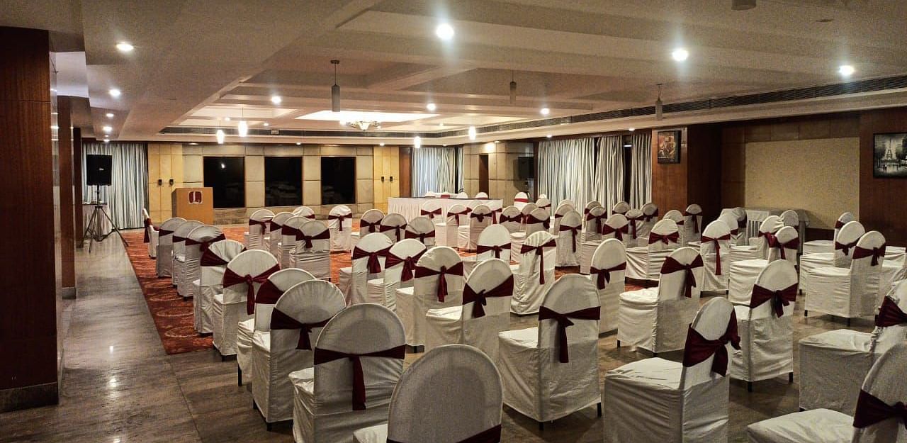 A large banquet hall with rows of chairs arranged, bright ceiling lights, and a clean, neat setup - Lords Plaza Ankleshwar
