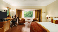 An image of a Deluxe Room featuring bed, flat screen TV, lamps, work desk, chair, sofa set and table - Ramada Plaza by Wyndham Palm Grove