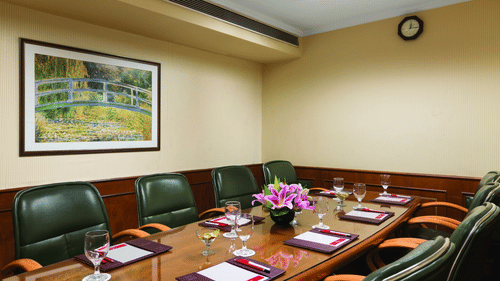 A large desk with green chairs below it inside the Business Centre at Hotel Ramada Plaza Palm Grove.