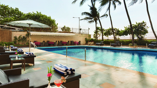 An image of the poolside patio with lounge chairs and palms trees in the background - Ramada Plaza by Wyndham Palm Grove
