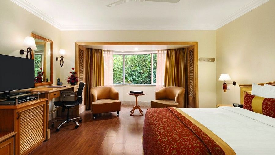 An image of a Deluxe Room featuring bed, flat screen TV, lamps, work desk, chair, sofa set and table - Ramada Plaza by Wyndham Palm Grove