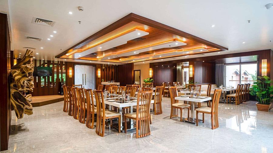 The spacious and brightly lit dining hall at Mansha Palace features numerous set tables and comfortable wooden chairs.