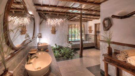 A minimalist bathroom vanity with a white vessel sink and a large round mirror set against stone walls at Earthitects.