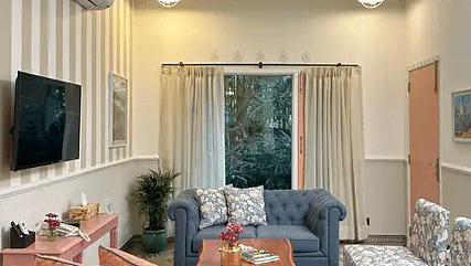 Cozy living room with a mix of blue and peach furniture, wall-mounted TV, and large windows overlooking greenery at Karma Chalets.