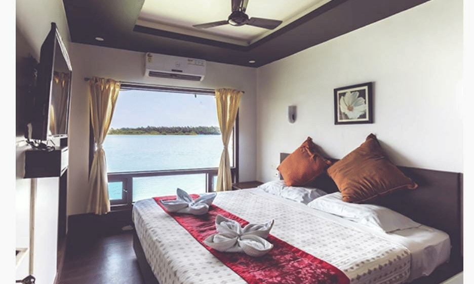 Bedroom with a queen bed, brown pillows, ceiling fan, and window view at Paradise Lagoon Resort, Udupi.