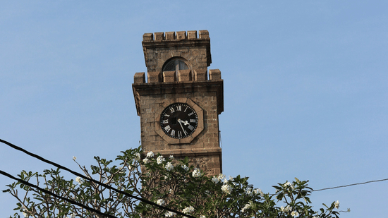View of the Galle Fort clock tower in Sri Lanka rising above lush green trees against a clear bright blue sky.