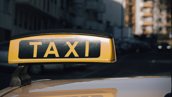 Taxi sign displayed on a vehicle in an urban street setting.