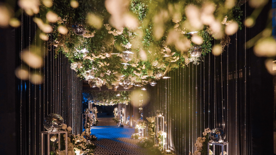A luxurious, dimly lit hallway at Ananta Spa & Resort, Jaipur, features a thick floral and foliage ceiling canopy with warm string lights.
