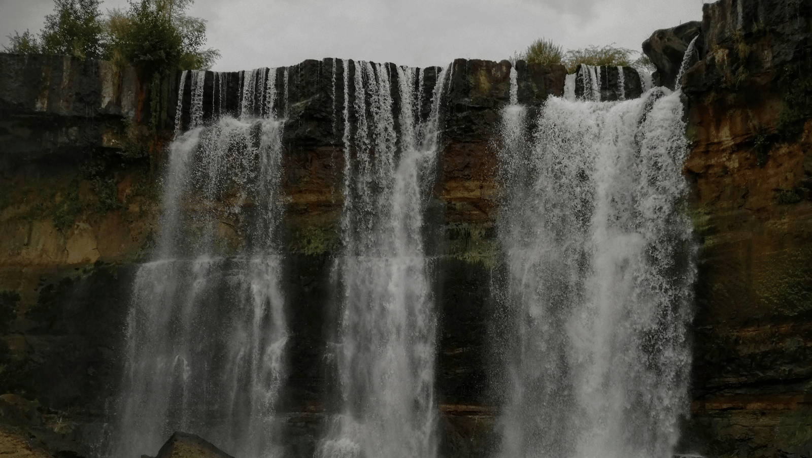 A waterfall with a gloomy sky above it.