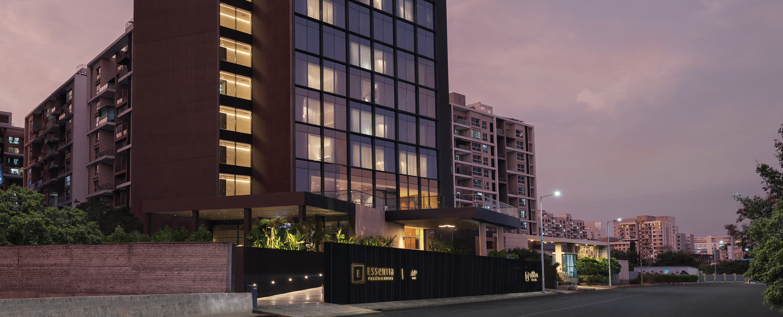 Facade view of Essentia Premiere, Pune, with lights on during twilight hour.