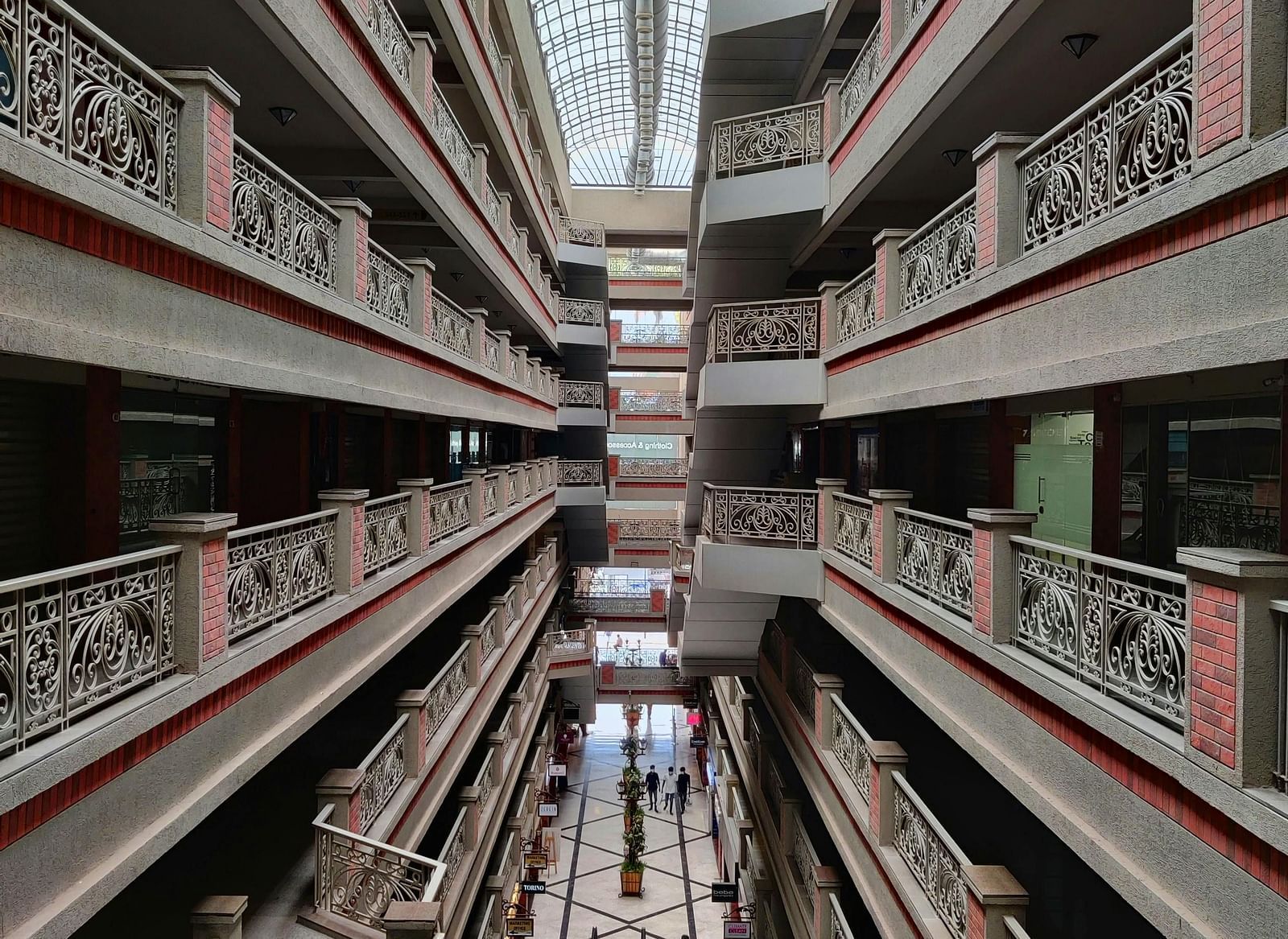 A vertical shot looking straight down through the center of a multi-story building with repeating balconies and escalators, topped with a glass ceiling.