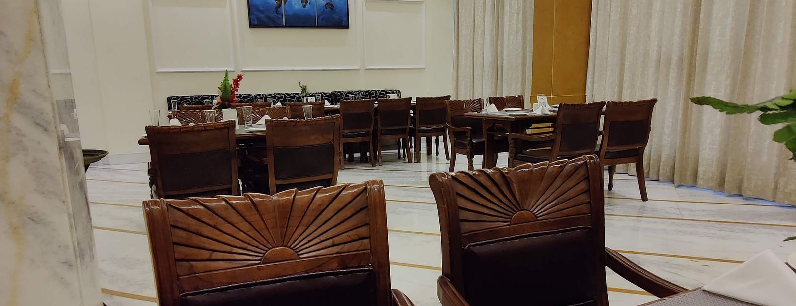 Two chairs facing the dining table along with plates and napkins in front of itCorner view shot of the dining area of the Gold Plate restaurant with central air-conditioning and a small cabinet in the corner of the restaurant - Hotel Gold, Panipat