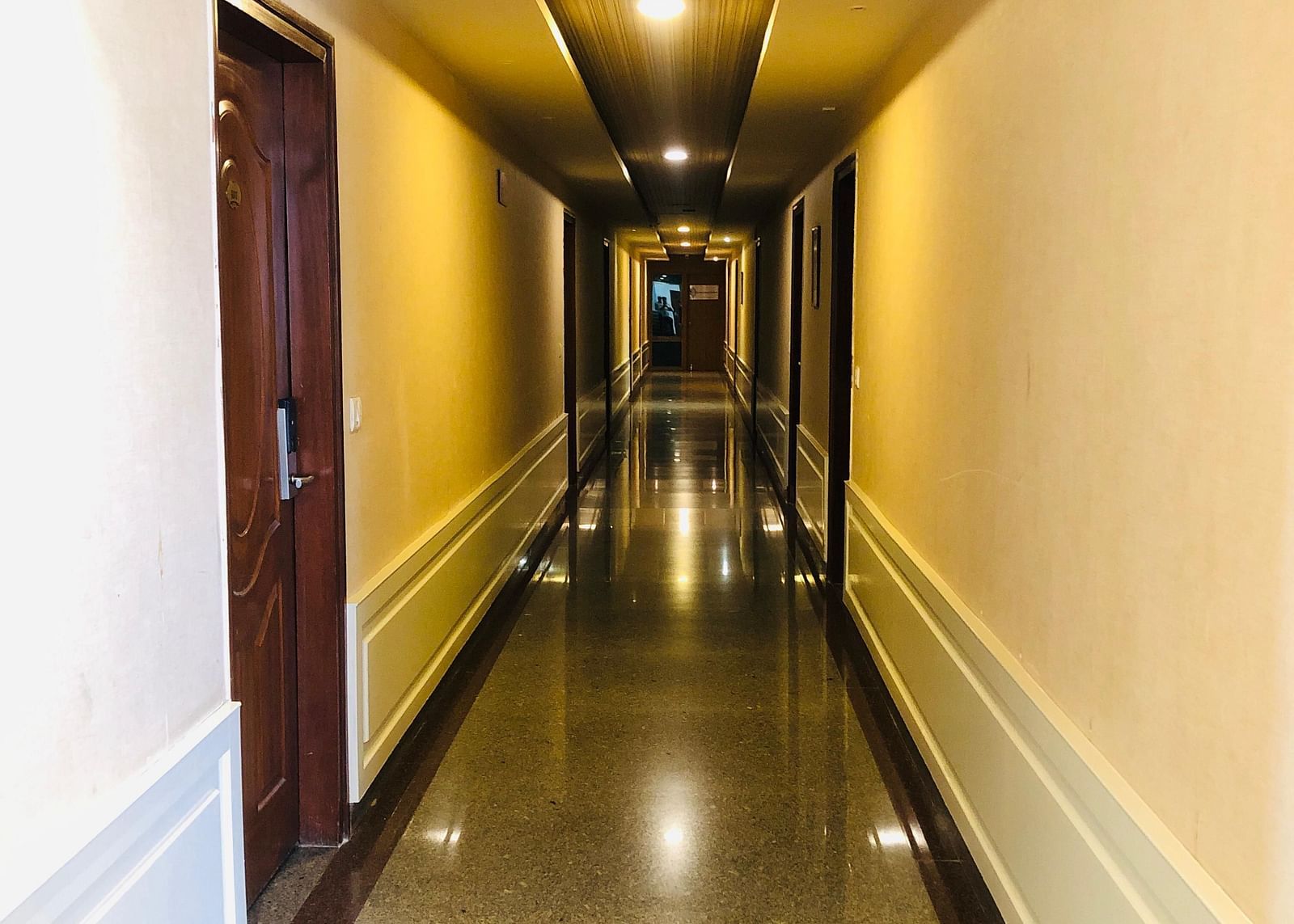 A well-lit hotel corridor with a polished floor, warm yellow lighting, and doors leading to guest rooms - Astra Hotels and Suites, HSR Sector 7