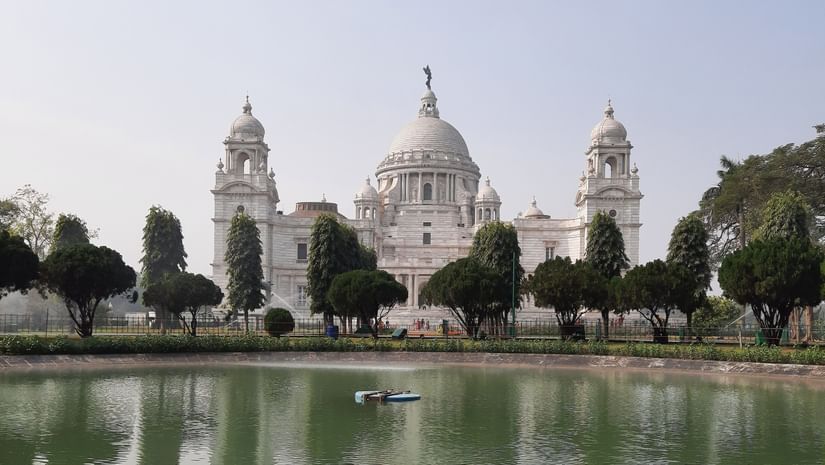 A far out view of Victoria memorial with roses in the foreground and a waterbody in between.