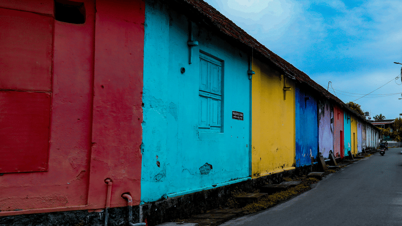 A view of colourful outdoor walls in Mattancherry next to the street with blue sky in the background.