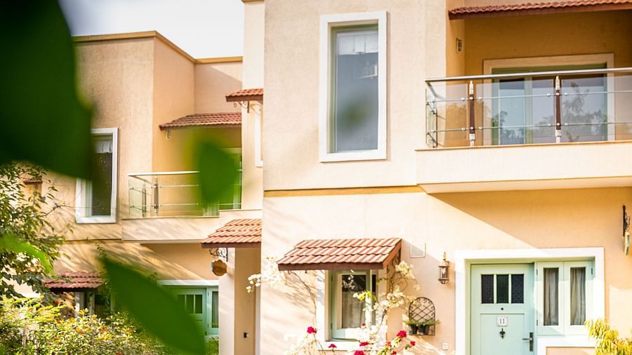 A man holding a camera amidst a garden with trees and plants, in front of a cream-coloured villa | Karma Chalets