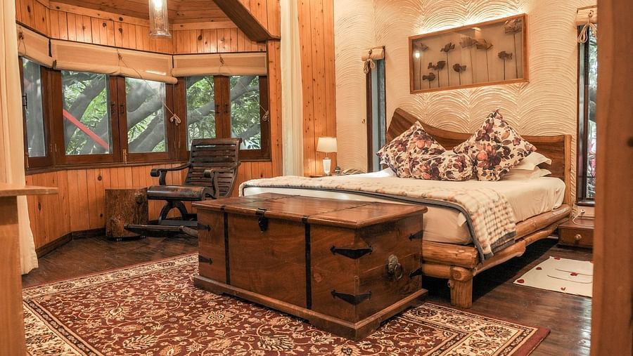 A bedroom with a patterned rug, a bed, and warm lighting, wooden interior - The Den Corbett Resort & Spa, Kumeria.