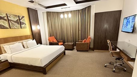 A spacious room with a large bed, cushioned seating beside the window with curtains, and a TV with a writing desk to the side | Cenneys Gateway