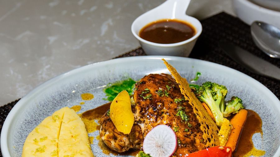 A plate of food with a piece of fish, vegetables, and a sauce, with a small bowl of liquid.