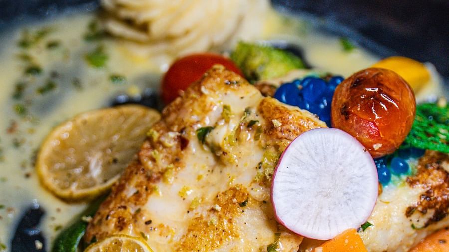 Fish with vegetables on a plate with sauce, showcasing a creamy texture and colorful elements.