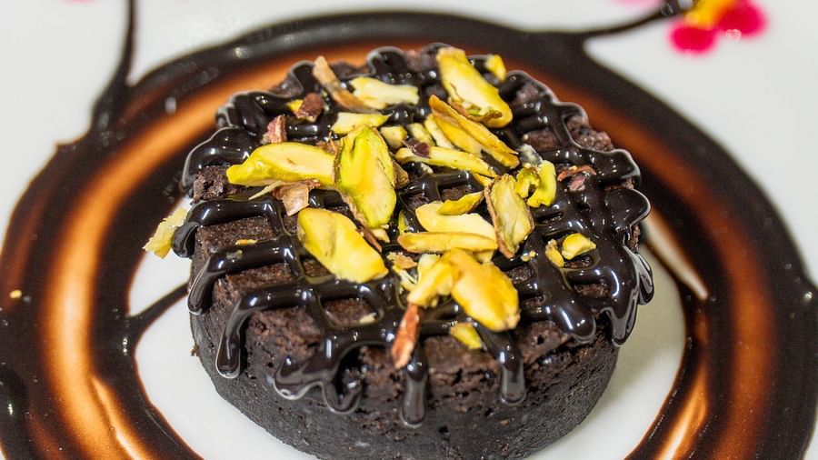 A plate with a dark dessert topped with golden flakes and decorative sauce.