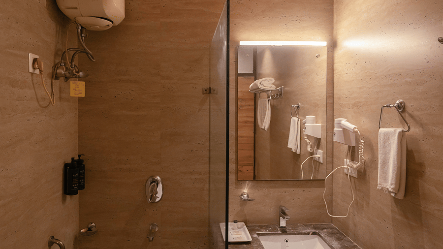 En-suite cottage bathroom with wooden ceiling accents, vanity wash basin, mirror, and toilet - Wood Castle Spa & Resort, Jim Corbett