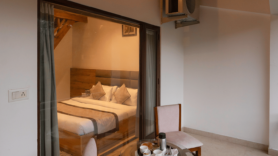 A cosy sitting area next to large glass sliding doors overlooking the private balcony of a resort room - Wood Castle Spa & Resort, Jim Corbett