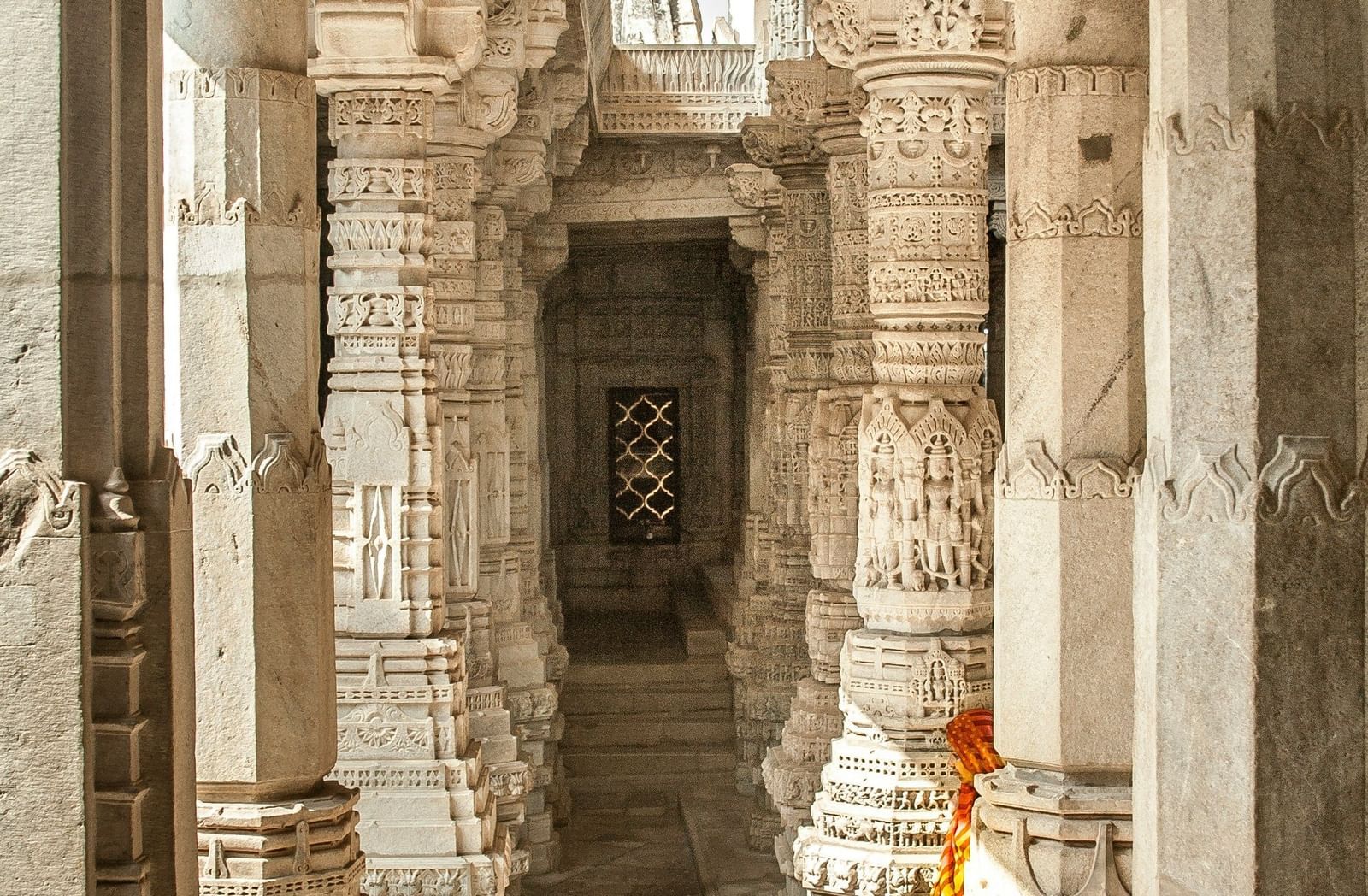  A hallway in a temple with a long corridor of intricately carved marble pillars, leading to an ornate window at the end.